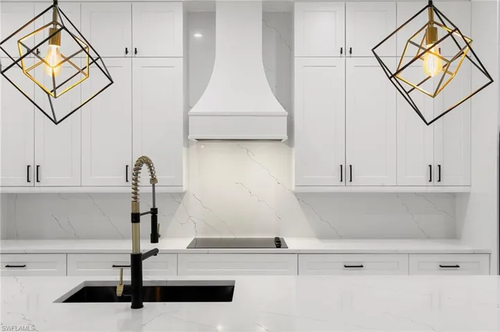 Interior details featuring sink, white cabinetry, custom range hood, decorative backsplash, and light stone countertops