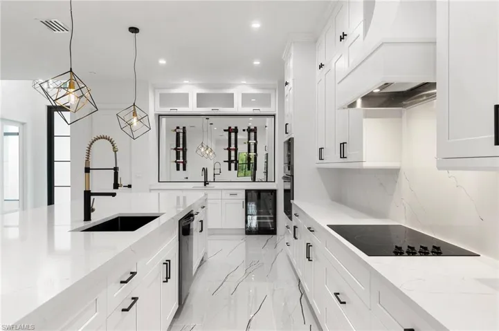 Kitchen featuring light stone counters, white cabinets, sink, black appliances, and custom range hood