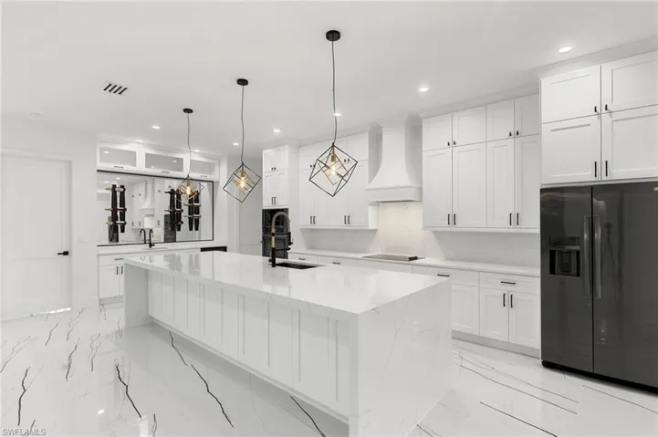 Kitchen featuring light stone counters, white cabinets, premium range hood, pendant lighting, and fridge with ice dispenser