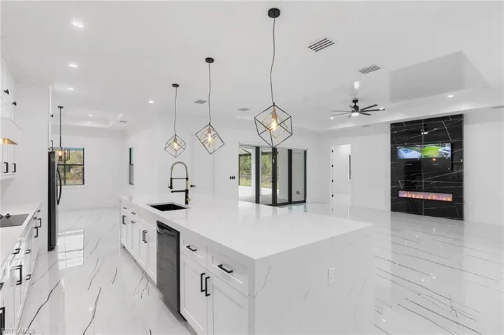 Kitchen with ceiling fan, hanging light fixtures, sink, a large island with sink, and black appliances