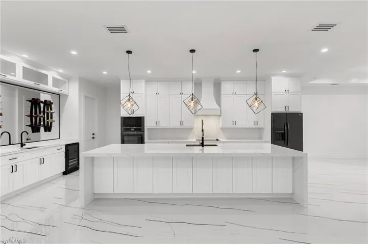 Kitchen featuring hanging light fixtures, premium range hood, black fridge, and a spacious island