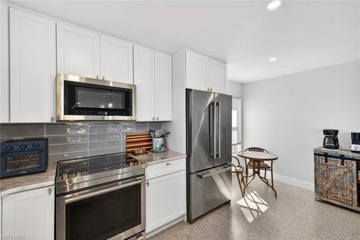 Kitchen featuring appliances with stainless steel finishes, white cabinetry, dark aggregate flooring, decorative backsplash, and recessed lighting