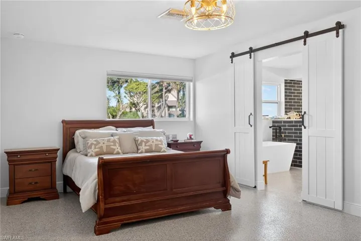 Bedroom with a barn door, speckled floor, and multiple windows