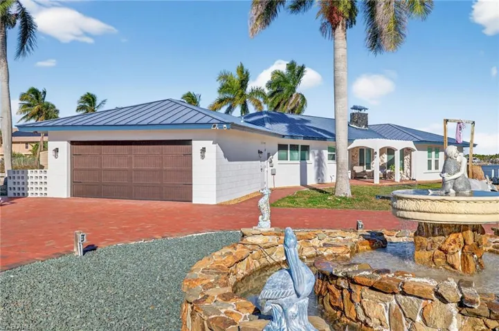 View of front of property featuring a standing seam roof, an attached garage, a metal roof, a chimney, and driveway