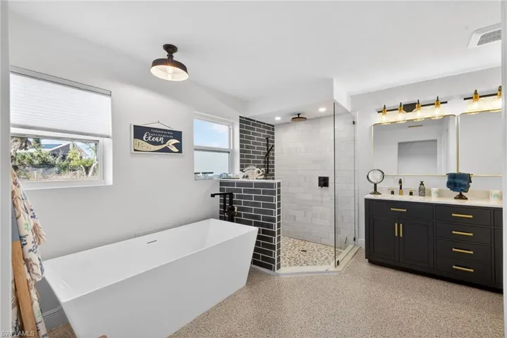 Full bathroom featuring vanity, a stall shower, a freestanding tub, and dark speckled floor