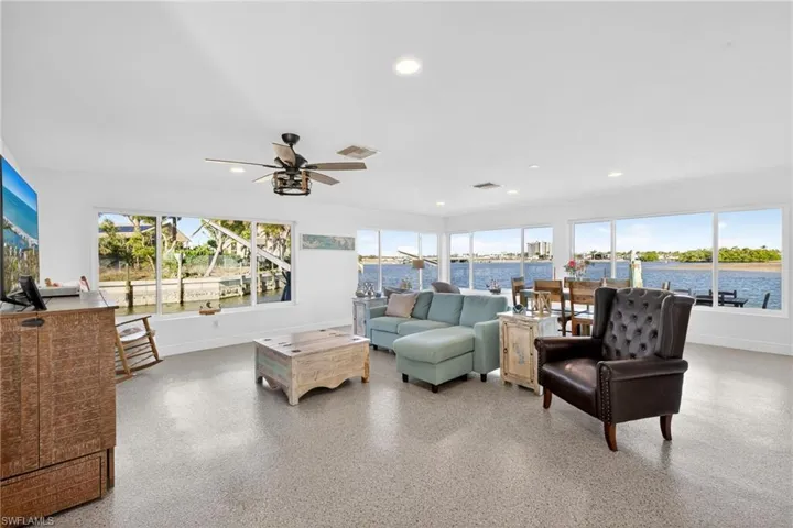Living area with plenty of natural light, dark speckled floor, recessed lighting, a ceiling fan, and a water view