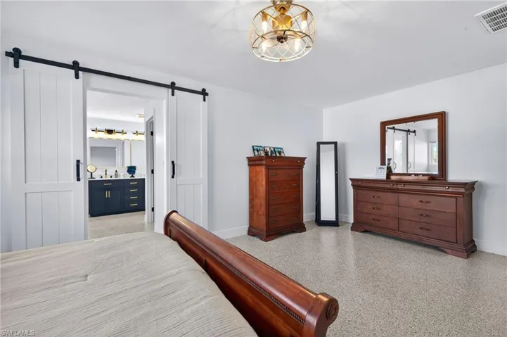 Bedroom with dark aggregate flooring, ensuite bath, and a barn door