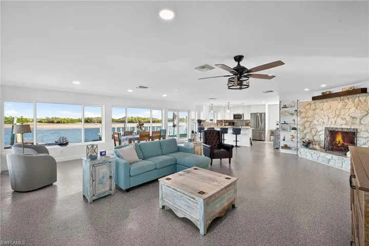 Living room featuring a stone fireplace, a water view, recessed lighting, a ceiling fan, and speckle patterned floor
