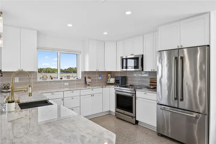 Kitchen featuring stainless steel appliances, dark aggregate flooring, white cabinetry, recessed lighting, and light stone countertops