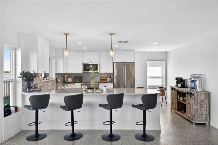 Kitchen featuring white cabinetry, a peninsula, a kitchen breakfast bar, light stone countertops, and appliances with stainless steel finishes