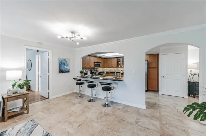Kitchen featuring arched walkways, brown cabinets, decorative backsplash, a kitchen bar, and crown molding