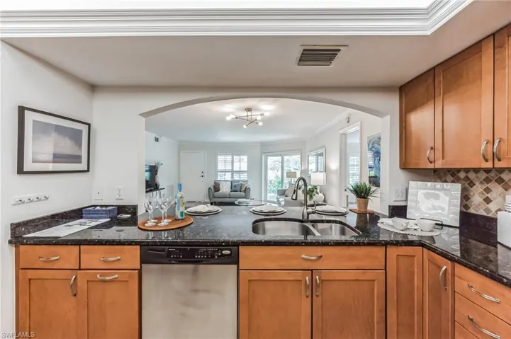 Kitchen with stainless steel dishwasher, crown molding, brown cabinetry, a peninsula, and dark stone counters