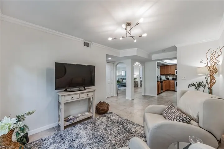 Living room featuring arched walkways, a chandelier, ornamental molding, and light tile patterned floors