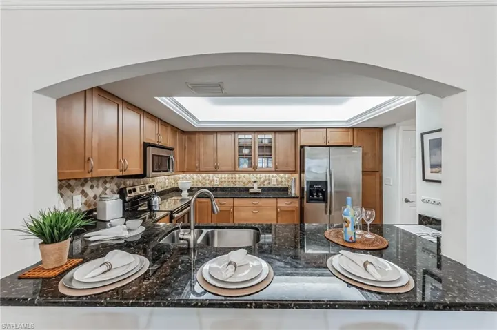 Kitchen featuring arched walkways, stainless steel appliances, brown cabinets, glass insert cabinets, and tasteful backsplash