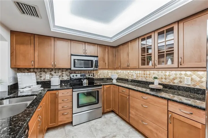 Kitchen featuring appliances with stainless steel finishes, glass insert cabinets, backsplash, and dark stone countertops