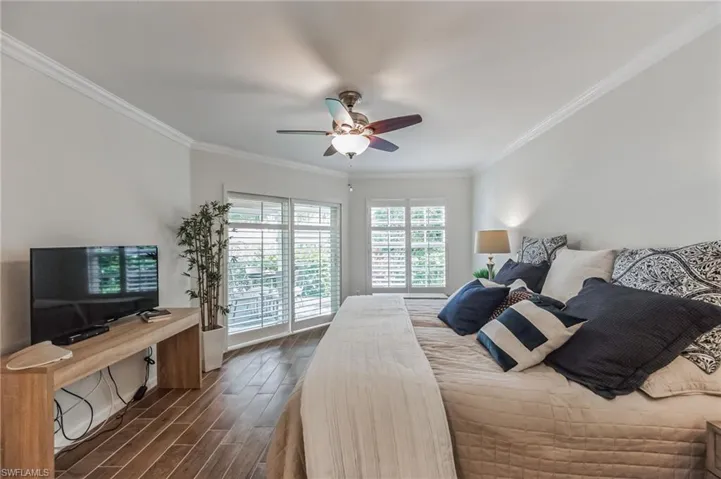 Bedroom with dark wood finished floors, ornamental molding, and ceiling fan