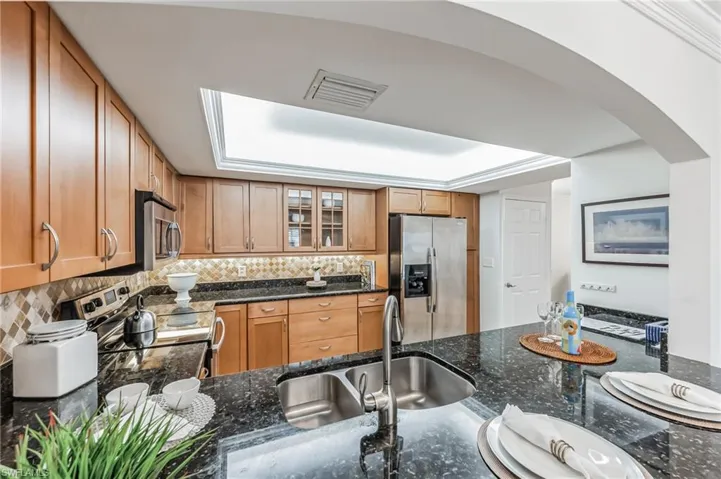 Kitchen featuring arched walkways, stainless steel appliances, glass insert cabinets, and dark stone counters
