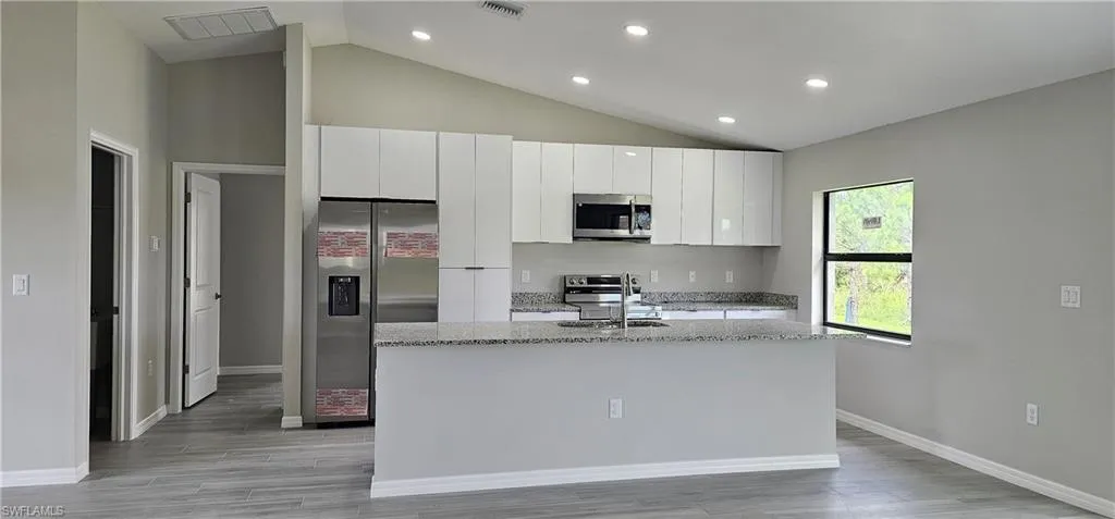 Kitchen featuring stainless steel appliances, an island with sink, white cabinetry, lofted ceiling, and light wood-style floors