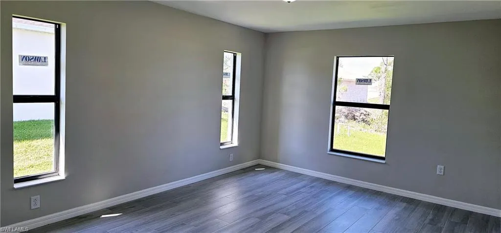 Empty room with dark wood-type flooring, a healthy amount of sunlight, and baseboards