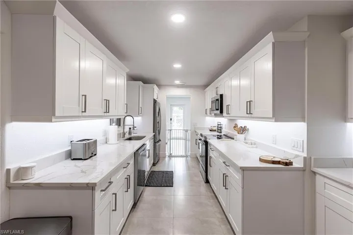 Kitchen featuring appliances with stainless steel finishes, white cabinetry, recessed lighting, light tile patterned flooring, and light stone countertops