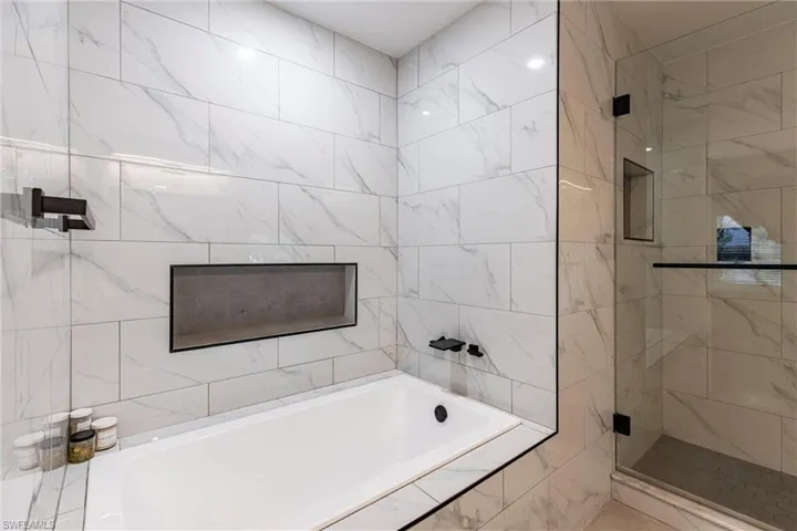 Full bath featuring a tile shower, a relaxing tiled tub, and tile walls