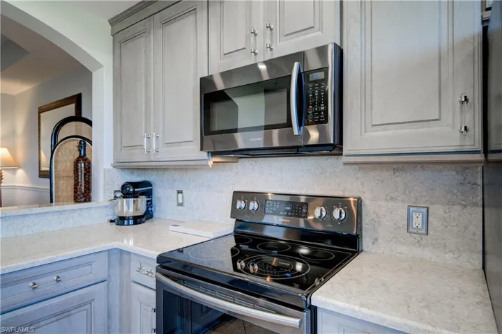 Kitchen with tasteful backsplash, black range with electric stovetop, gray cabinetry, and light stone counters