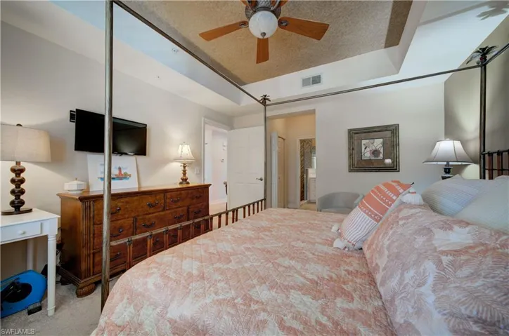 Bedroom with a textured ceiling, light colored carpet, ceiling fan, and a tray ceiling