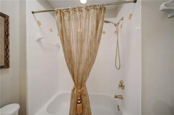 Bathroom featuring toilet and shower / bathtub combination with curtain
