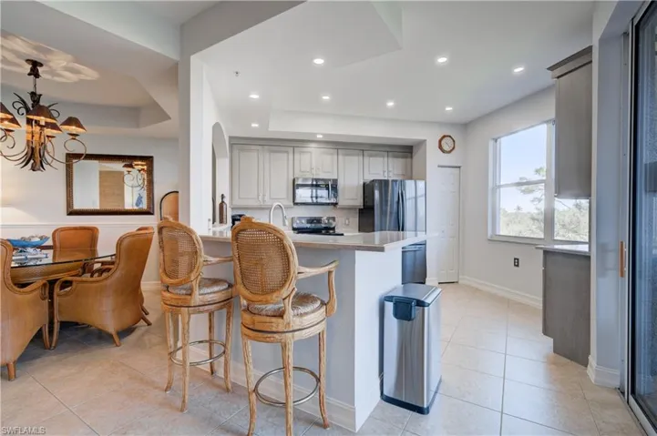 Kitchen with decorative backsplash, appliances with stainless steel finishes, kitchen peninsula, a tray ceiling, and a chandelier