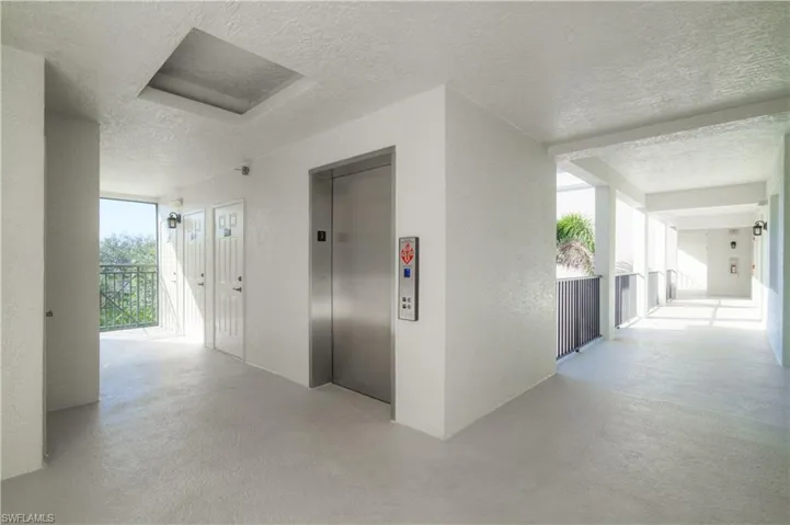 Corridor featuring a textured ceiling, elevator, and light colored carpet