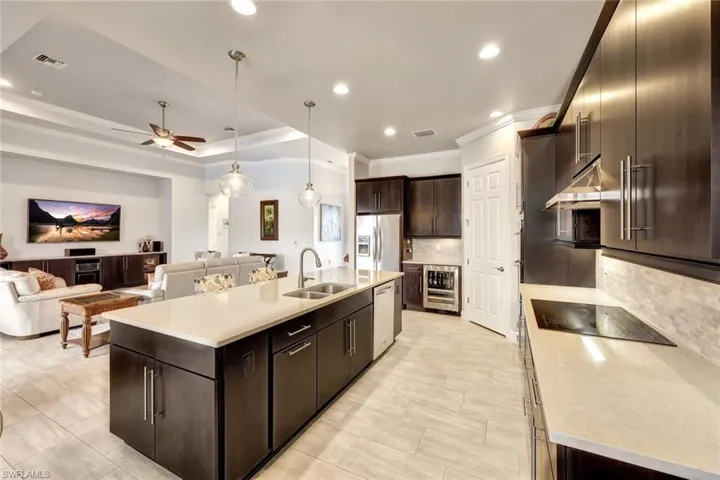 Kitchen featuring sink, a kitchen island with sink, dark brown cabinets, tasteful backsplash, and beverage cooler