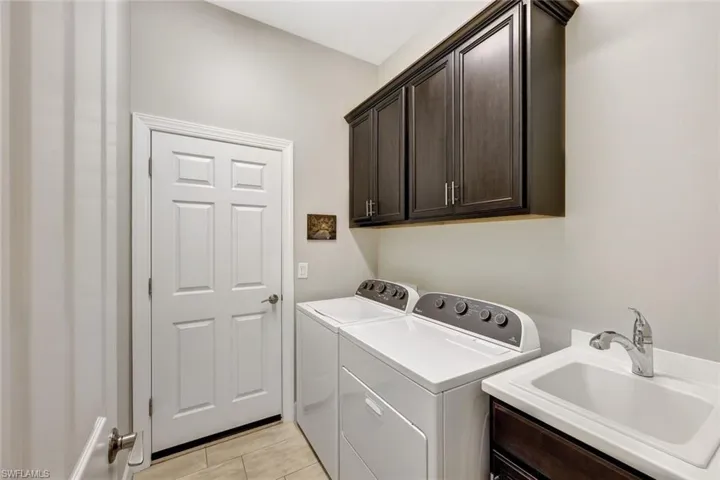 Clothes washing area featuring sink, light tile patterned floors, washer and clothes dryer, and cabinets
