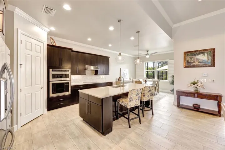 Kitchen with dark brown cabinetry, sink, hanging light fixtures, a center island with sink, and appliances with stainless steel finishes