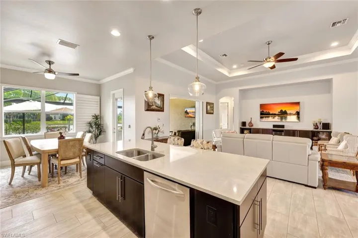 Kitchen featuring sink, hanging light fixtures, a kitchen island with sink, stainless steel dishwasher, and a raised ceiling