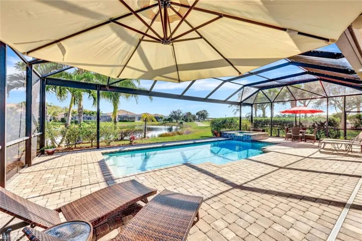 View of swimming pool with an in ground hot tub, a water view, glass enclosure, and a patio