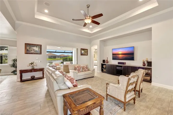Living room with a raised ceiling, crown molding, and ceiling fan