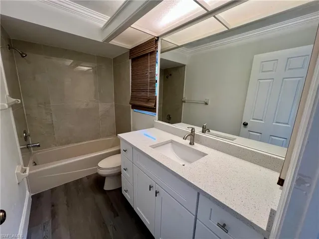 Full bathroom featuring vanity, crown molding, tiled shower / bath combo, toilet, and luxury vinyl plank flooring.