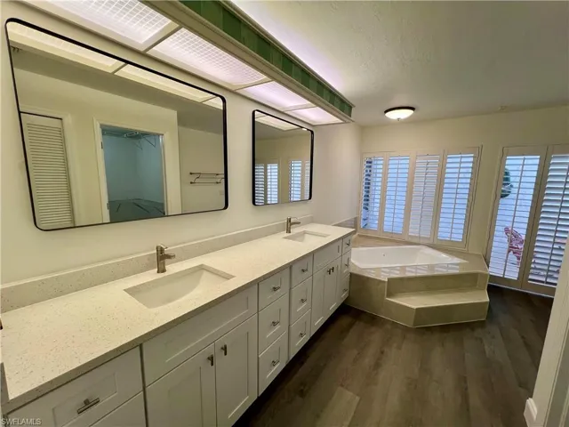 Primary Bathroom with tiled tub, dual sinks and  vanity, and hardwood / wood-style flooring