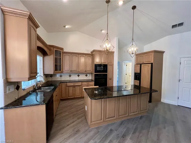 Kitchen GRANITE TOPS with sink, black appliances, a center island, and hanging light fixtures