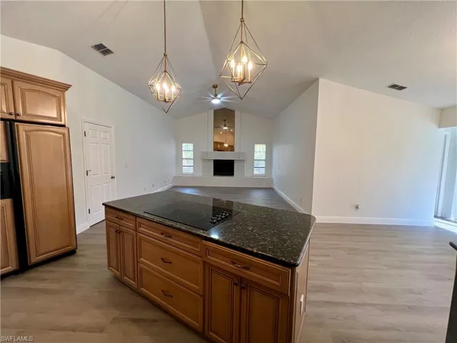 Kitchen featuring light wood-type flooring, black electric cooktop, vaulted ceiling, decorative light fixtures, and a center island with GRANITE TOPS.