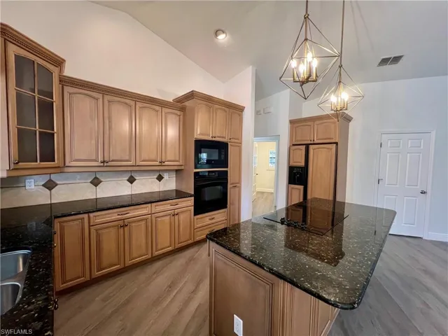 Kitchen with tasteful backsplash, GRANITE countertops, pendant lighting, and black appliances