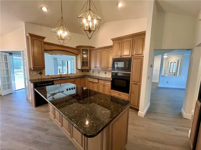 Kitchen featuring GRANITE TOPS, tasteful backsplash, hanging light fixtures, black appliances, and sink
