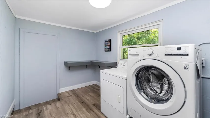 Laundry area with washer and dryer, light wood-style floors, and ornamental molding