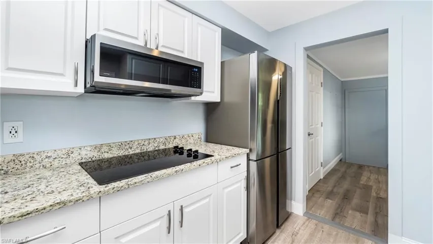 Kitchen with stainless steel microwave, white cabinetry, light stone countertops, light wood-style floors, and black electric cooktop