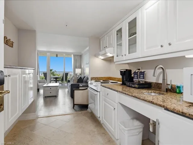 Kitchenette featuring white cabinetry, a light-toned patterned countertop, stainless steel sink with a gooseneck faucet, and a range hood