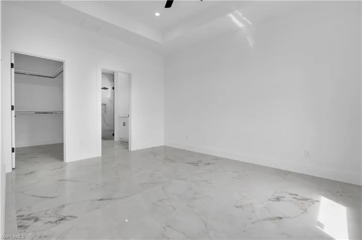 Spacious room featuring large format marble-look tile flooring, white baseboards, and a tray ceiling with recessed lighting