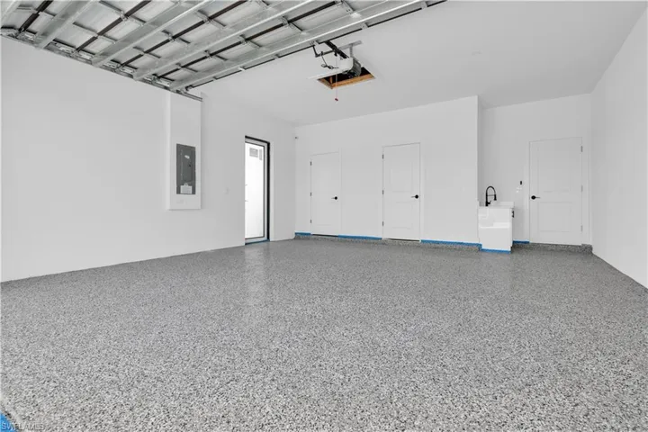 Spacious garage featuring a speckled epoxy floor, white painted walls, and multiple entry doors