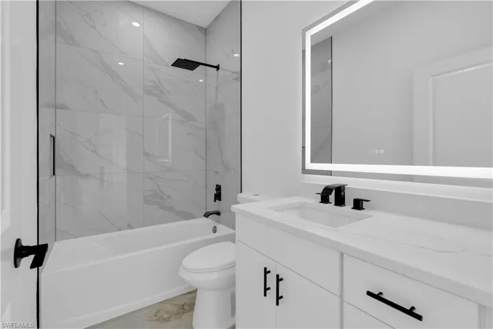 Modern bathroom featuring a white vanity with integrated sink, black matte fixtures, and a lighted mirror