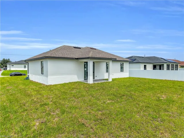 Rear exterior showcasing a covered patio, white stucco finish, dark shingle roof, and a grassy backyard