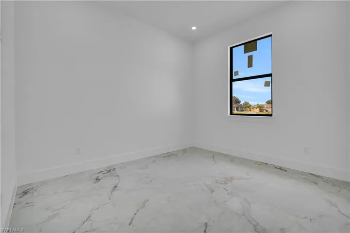 Spacious interior featuring marble-look tile flooring, crisp white walls, recessed lighting, and a prominent window with dark framing